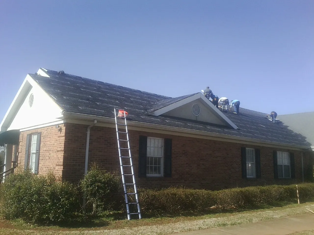 Crew tearing shingles off a brick ranch roof with a ladder set — Emergency Roof Repair work by our crew in Dry Ridge