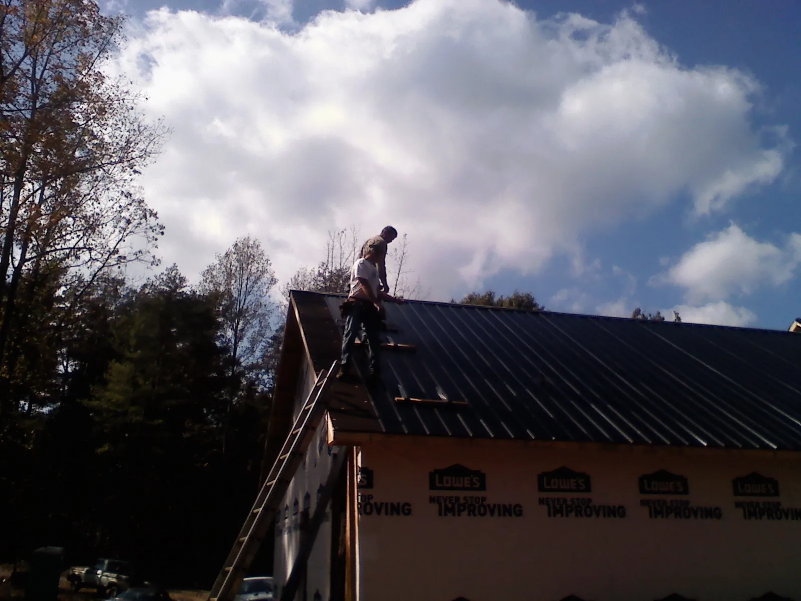 Roofer fastening dark metal panels high against a cloudy sky, from a Roof Inspection job in Dry Ridge