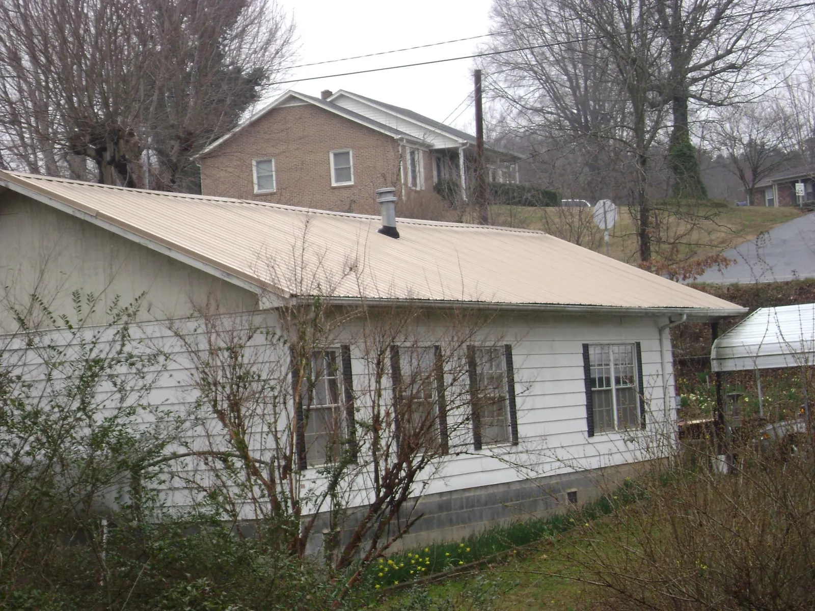 Tan metal roof on a white sided house set into a hillside — Commercial Roofing by Roofing Brothers in Dry Ridge